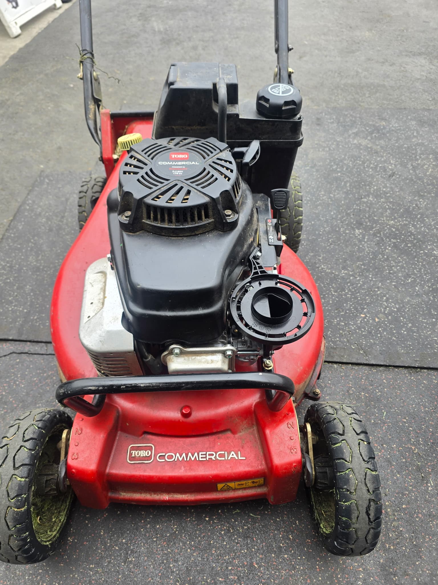 Red Toro Commercial walk-behind lawn mower with a black engine on a dark paved surface.